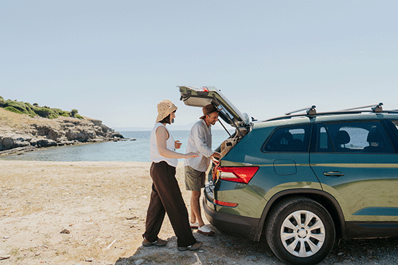 couple looking in the trunk of their car at the beach
